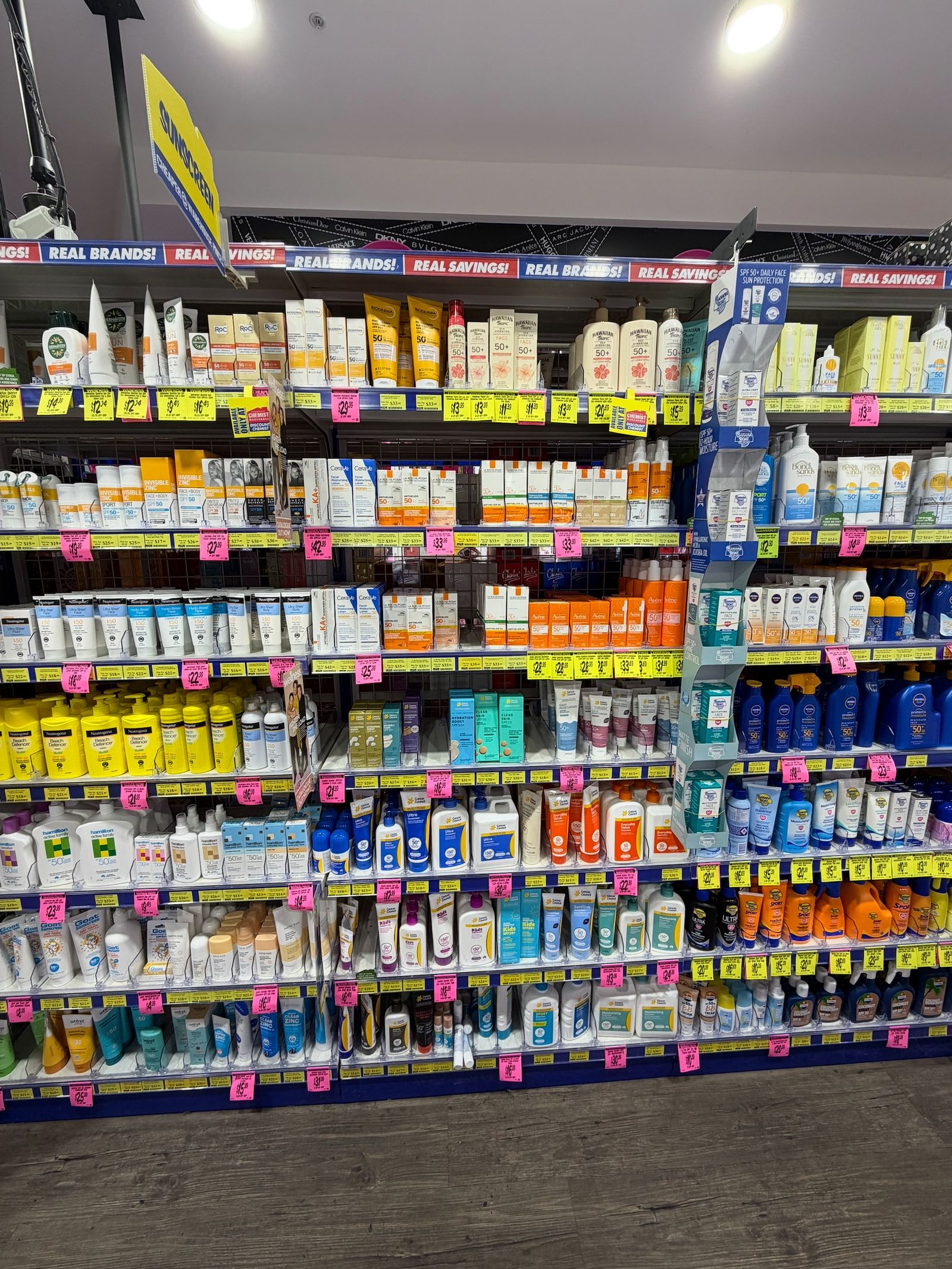 A retail sun-care shelf arranged in clear product rows with visible shelf labels
